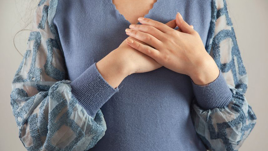 Person wearing a blue top with patterned sleeves holds both hands over their chest.