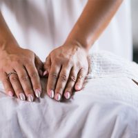 Close-up of a person’s hands performing a gentle massage on someone lying down, covered by a white sheet.