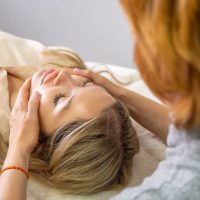 Person lying on a table receiving a facial massage from another individual in a calm setting.