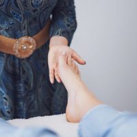 Person in patterned dress touching another person’s bare feet during a wellness or reflexology session.