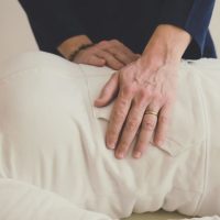 Person lying down while another person places hands on their abdomen, possibly performing a physical assessment.